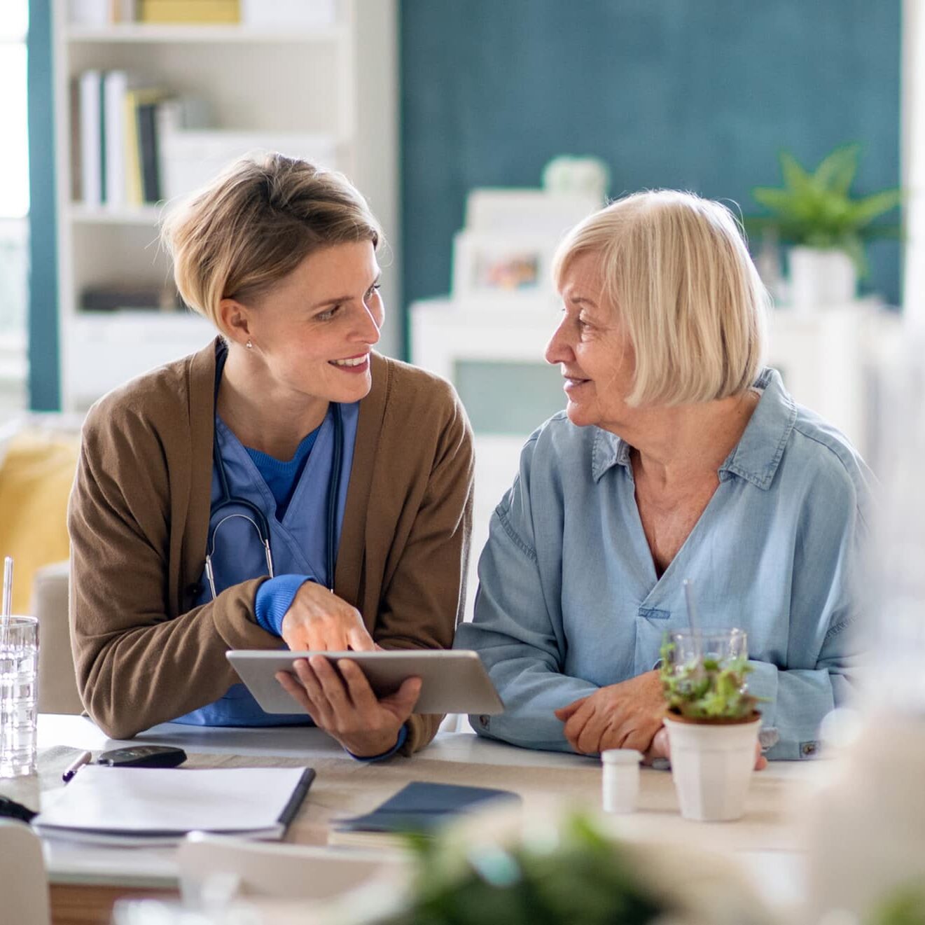 Caregiver or healthcare worker with senior woman patient, using a tablet and explaining.